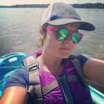 Woman in kayak wearing pink sunglasses with teal lenses.